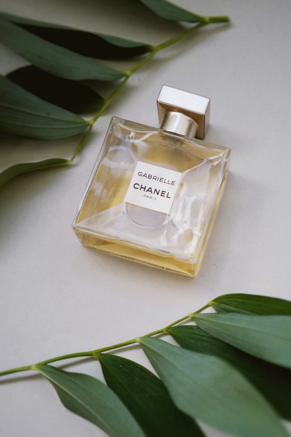A photo of a bottle of perfume surrounded by leaves